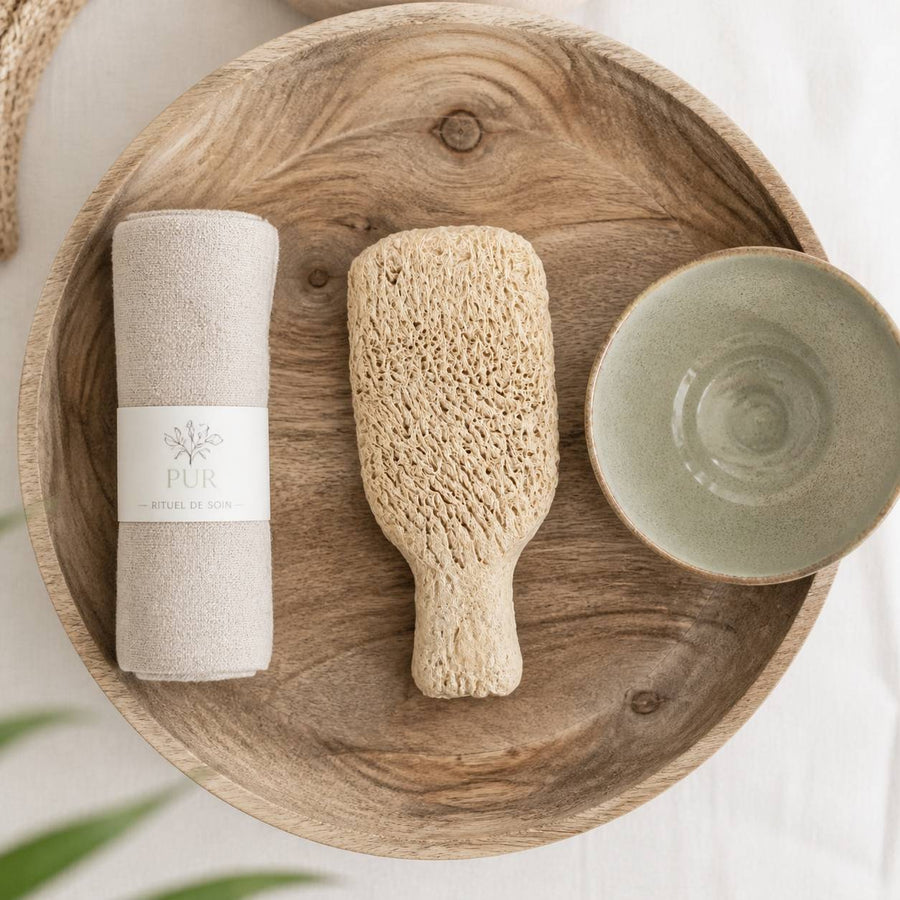 Grattoir Gommage en Terre Cuite – rituel d'utilisation vu du dessus, ambiance naturelle zen